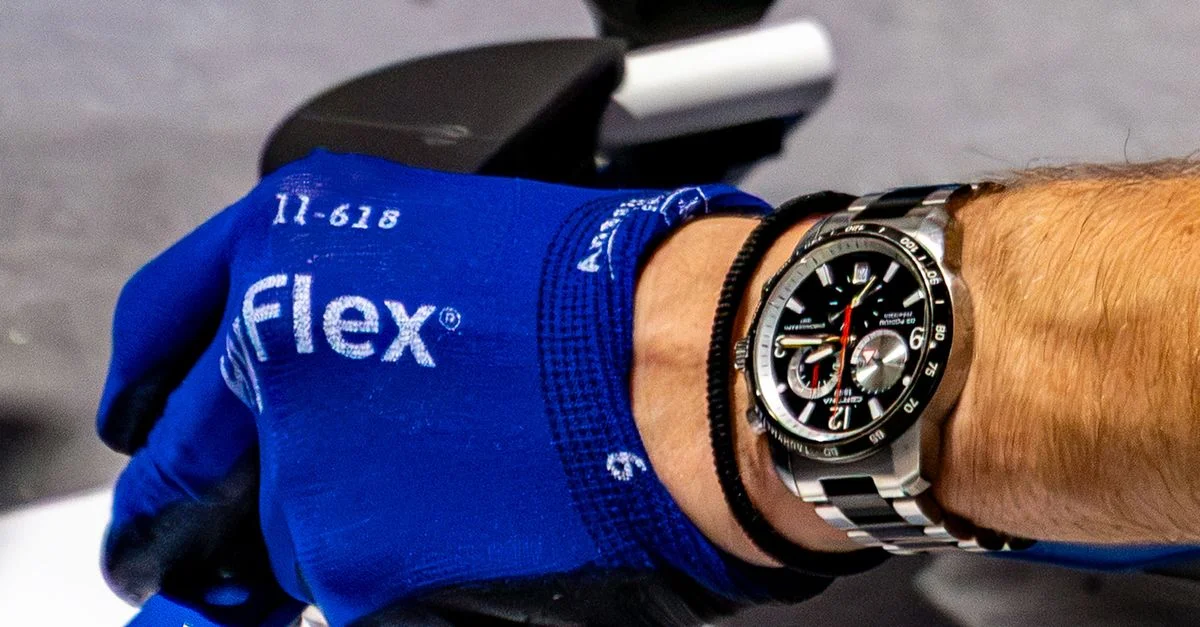 Primer plano del brazo de un hombre que lleva un guante de trabajo azul y un reloj de pulsera, centrándose en los detalles del reloj.
