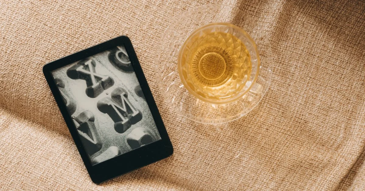 Una toma plana de un lector de e-book y una taza de té sobre una superficie texturizada de arpillera.
