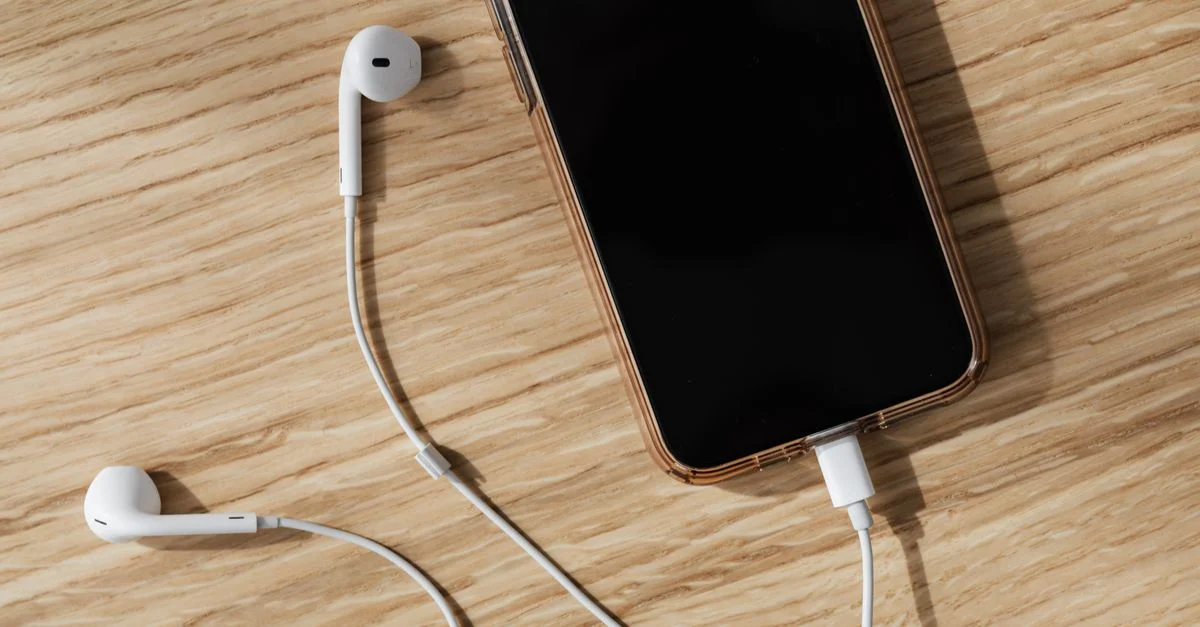 Un smartphone y auriculares colocados en una mesa de madera, con diseño moderno y estilo minimalista.