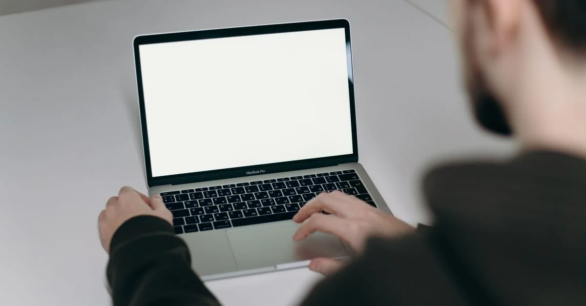 Un hombre escribiendo en un portátil con pantalla en blanco en casa, ilustrando el teletrabajo.