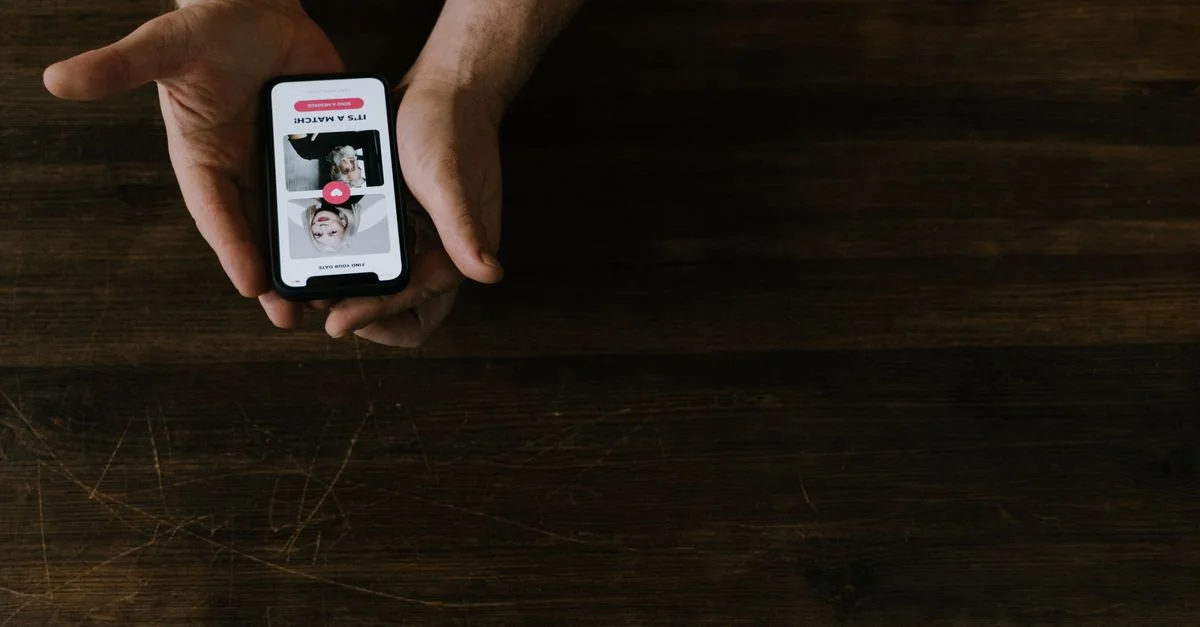 Acercamiento de manos sosteniendo un smartphone con una aplicación de redes sociales abierta sobre una mesa de madera.