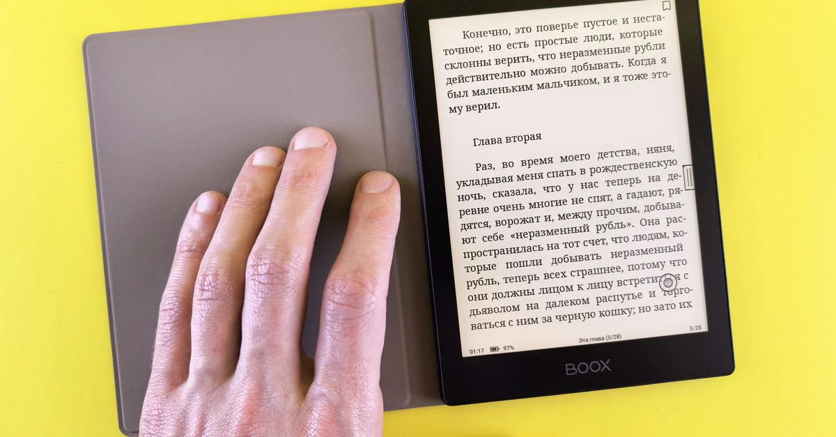 Una mano sosteniendo un lector electrónico que muestra texto sobre un fondo amarillo brillante, destacando la lectura digital moderna.