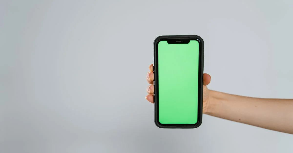 Primer plano de una mano sosteniendo un smartphone con pantalla verde, ofreciendo amplio espacio para texto.