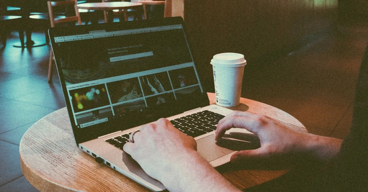 Persona usando un portátil en un acogedor café, destacando el estilo de vida del trabajo remoto con una taza de café en la mesa.