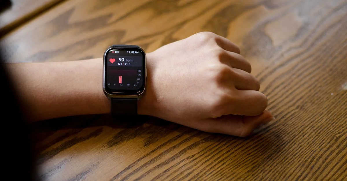 Primer plano de un reloj inteligente mostrando una frecuencia cardíaca de 90 bpm en la muñeca de una persona.