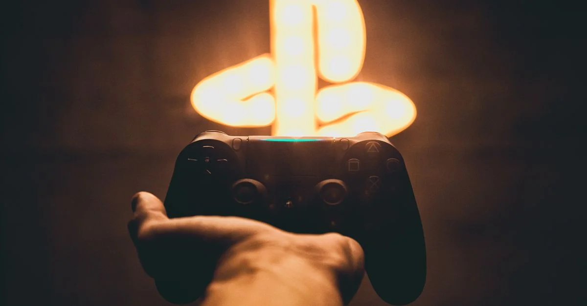 Una mano sostiene un mando de videojuegos con un símbolo de juego de neón brillante de fondo, creando un ambiente de juego vibrante.