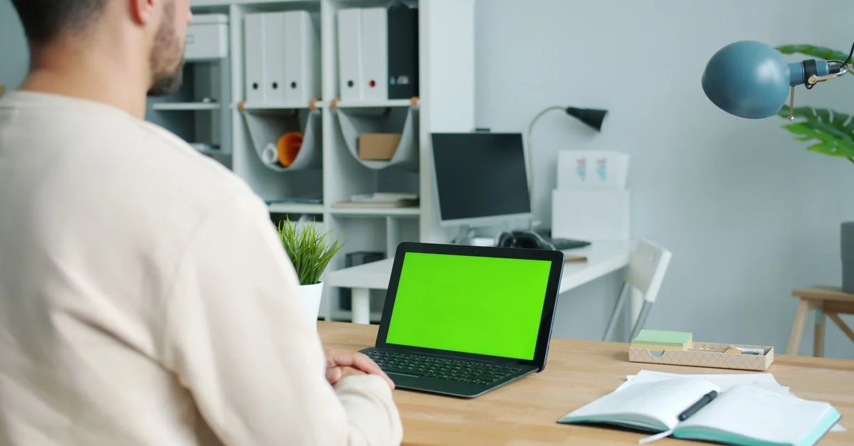 Configuración de una oficina en casa con un hombre usando una computadora portátil con pantalla verde.