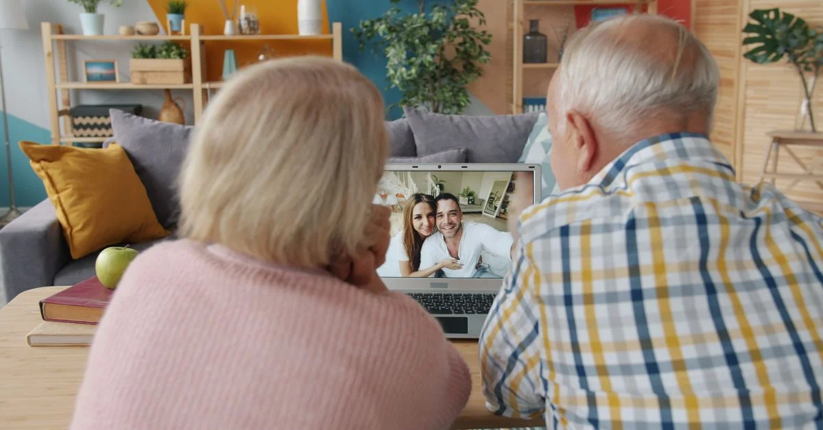 Una pareja de ancianos realiza una videollamada a su familia desde su portátil en un acogedor salón.