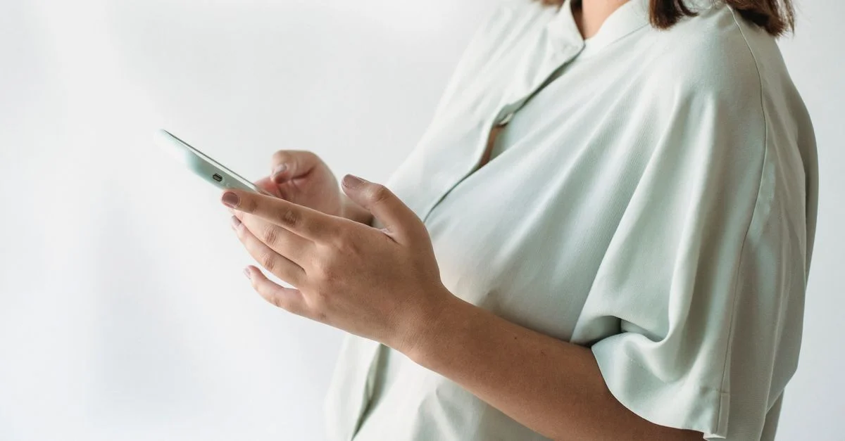 Una mujer con una camisa clara usando un teléfono inteligente en interiores, enfoque en la interacción tecnológica.