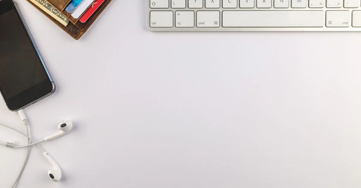 Disposición plana de un escritorio minimalista que presenta un smartphone, teclado, auriculares y cartera para inspirar productividad.