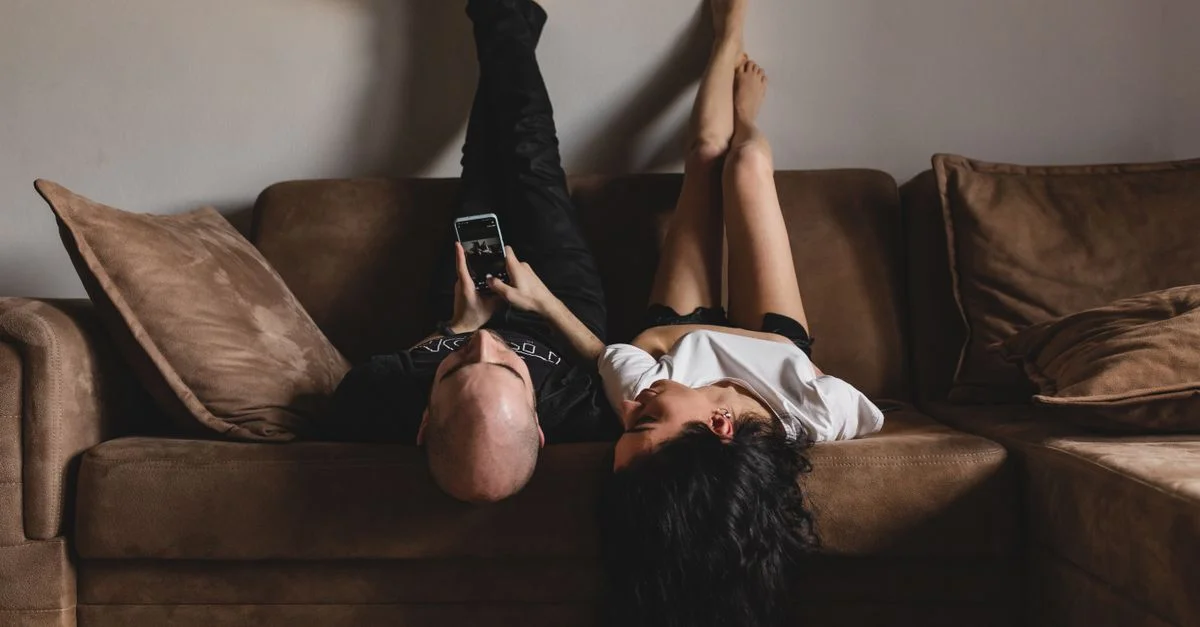 Una pareja disfrutando de un momento relajado en el sofá, usando un smartphone juntos en el interior.