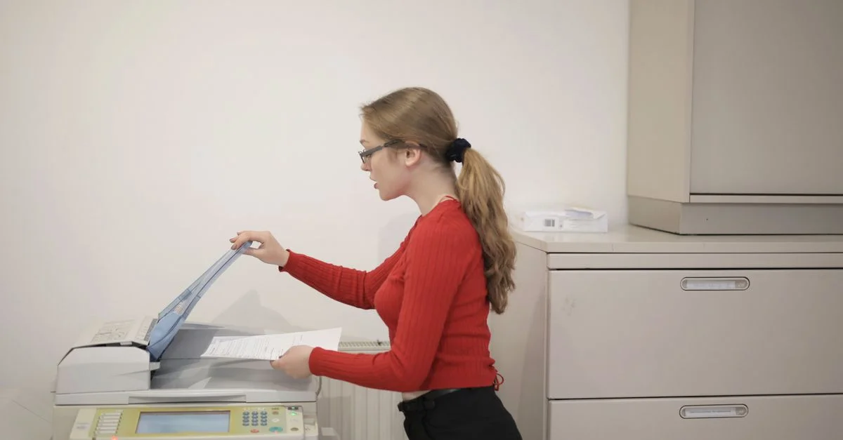 Una empleada de oficina utilizando una fotocopiadora para copiar documentos en interiores.