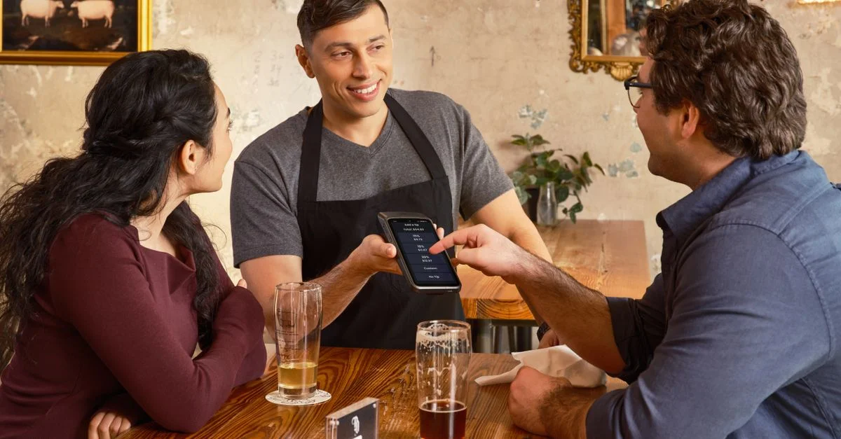Clientes interactuando con un sistema de pago digital en un restaurante acogedor y rústico.