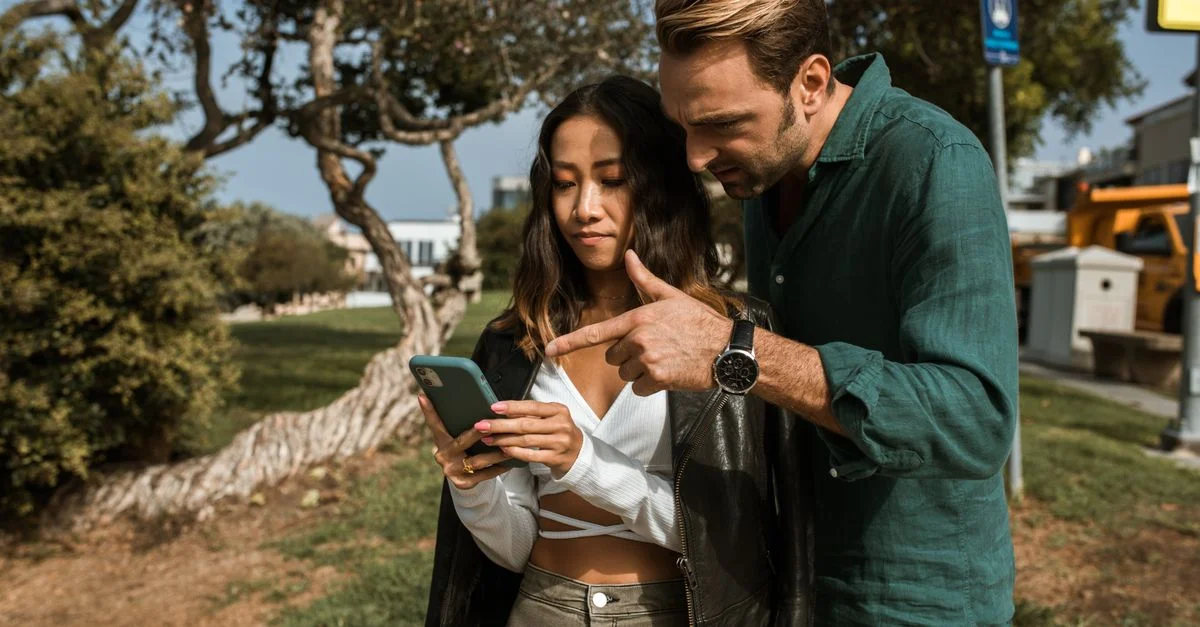 Un hombre y una mujer usando un teléfono inteligente juntos en un parque de la ciudad durante el día.