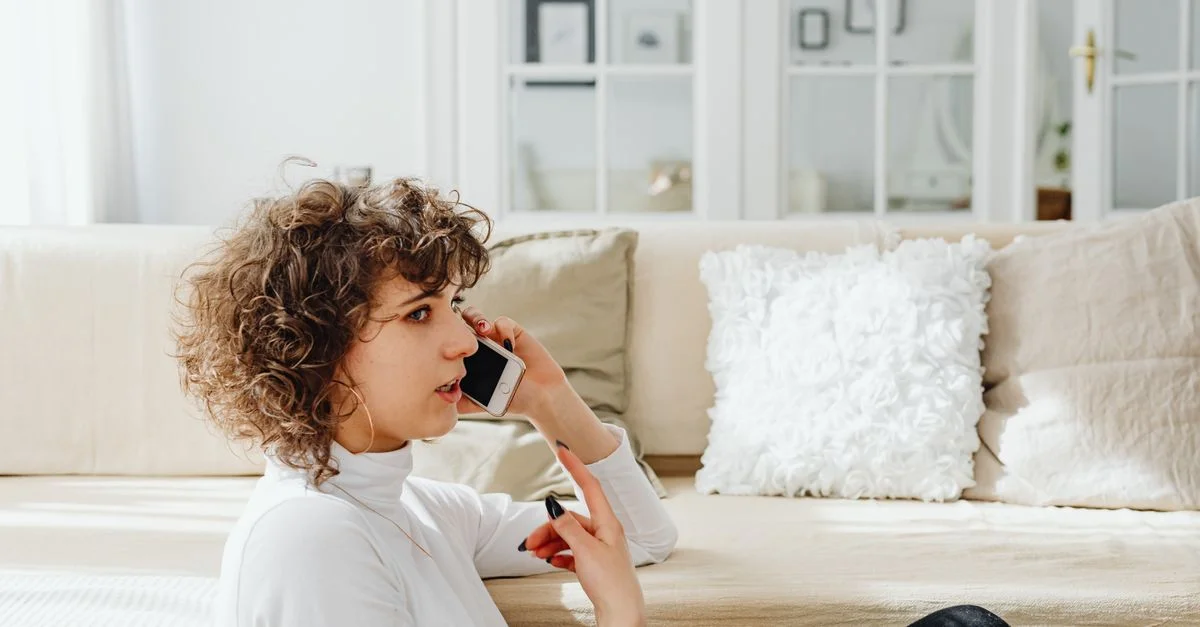 Una mujer está sentada, hablando por su teléfono en una sala de estar luminosa y acogedora.