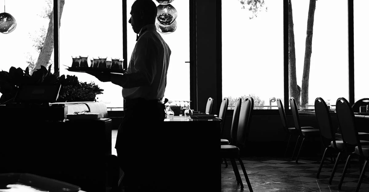 Silueta en blanco y negro de un camarero sirviendo bebidas en un elegante restaurante de Estambul. Ambiente artístico y melancólico.