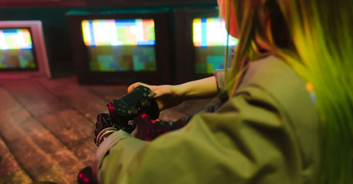 Una mujer con una mano prostética jugando a videojuegos en interiores entre televisores vintage, mostrando innovación y ocio.