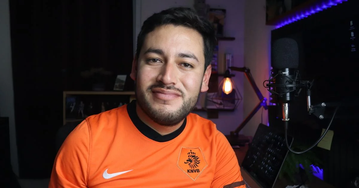 Retrato de un hombre sonriente en un estudio en casa con un micrófono, mostrando creatividad y comodidad.