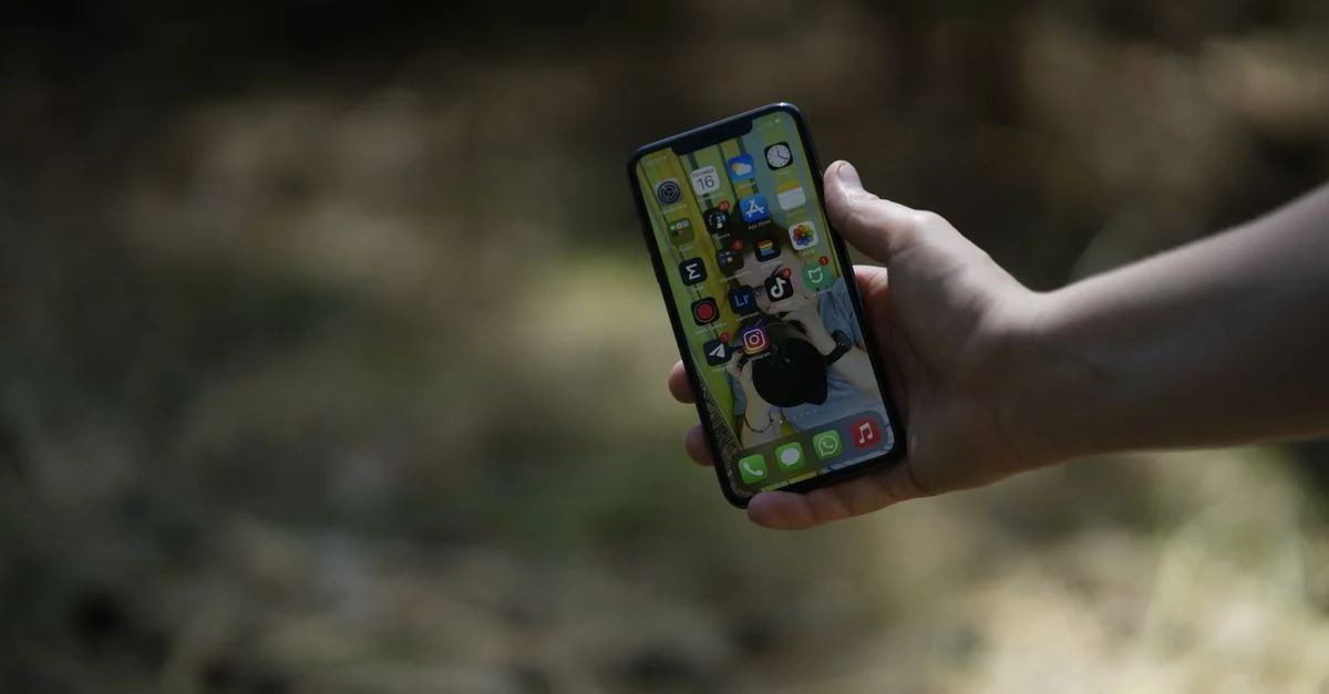 Una imagen en primer plano de una mano sosteniendo un smartphone al aire libre, con un fondo natural.