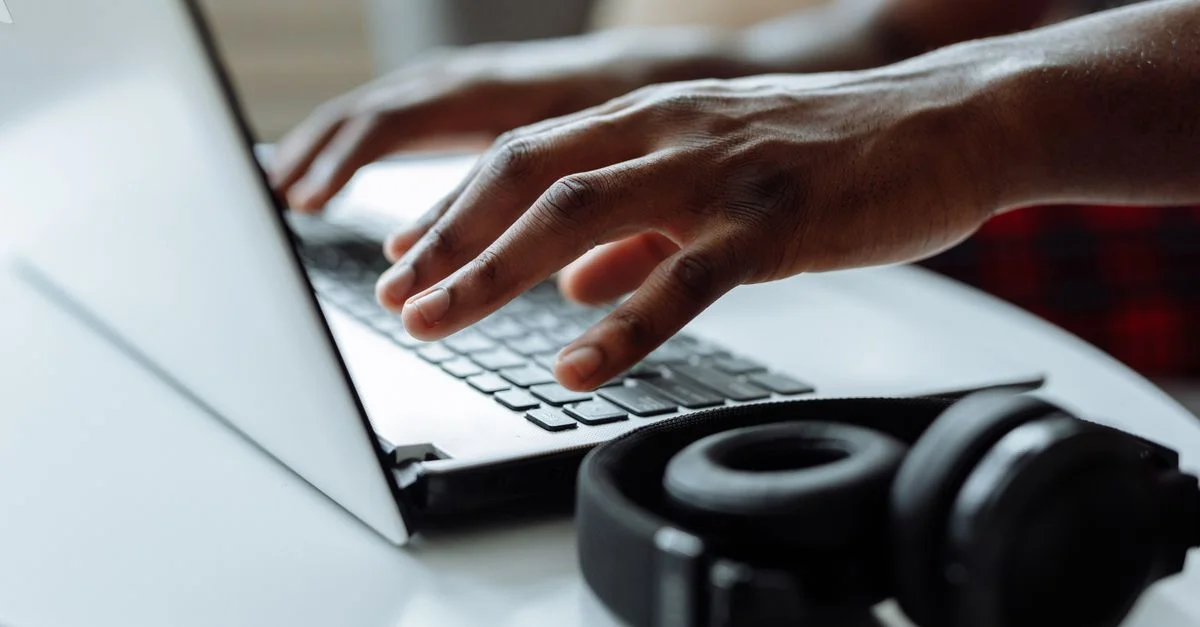Una persona escribiendo en un ordenador portátil con auriculares sobre una mesa, ideal para conceptos de trabajo remoto.