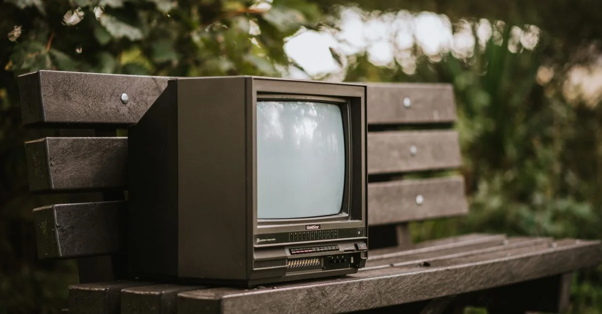 Un televisor retro colocado en un viejo banco de madera en un entorno natural exuberante.