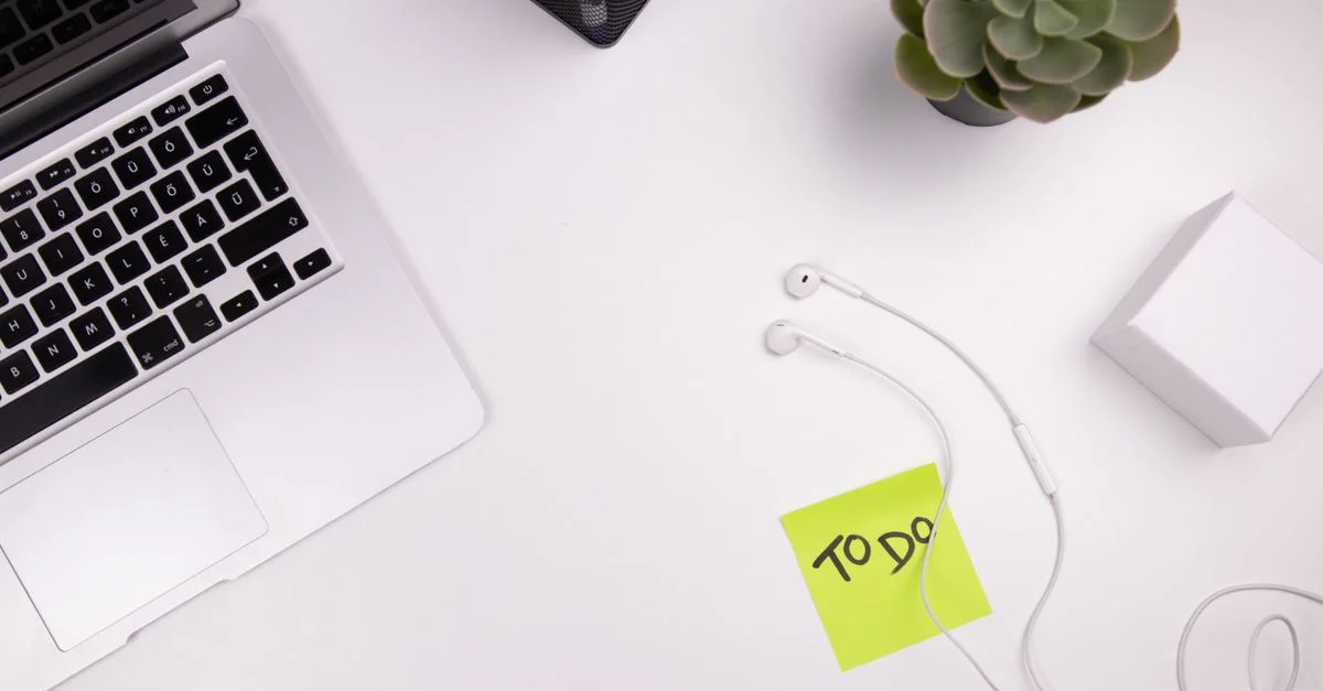 Espacio de trabajo organizado con un portátil, auriculares y una lista de tareas con decoración de plantas.