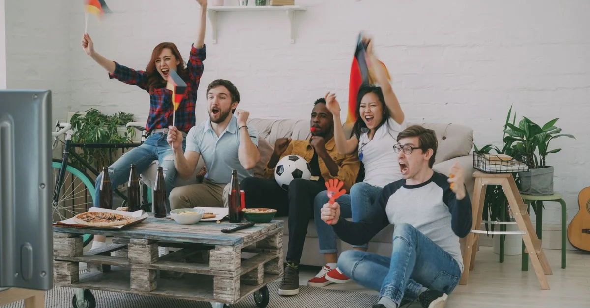 Grupo de amigos celebrando mientras ven un partido de fútbol en vivo en interiores.