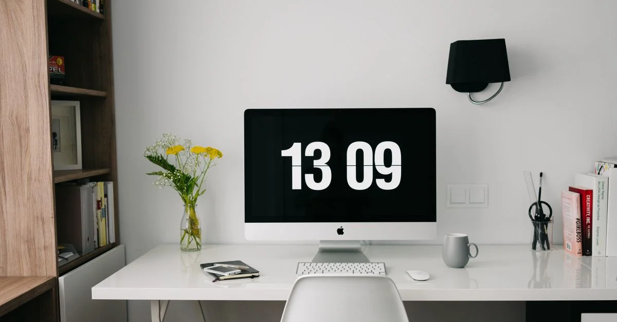 Un espacio de trabajo minimalista con un ordenador que muestra la hora, estanterías organizadas y una decoración elegante.