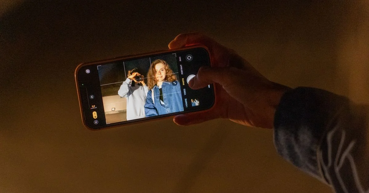 Una pareja capturando un recuerdo romántico con la cámara de un smartphone durante la noche en interiores.