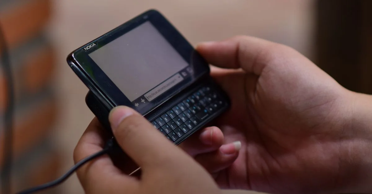 Manos operando un teléfono móvil vintage con teclado deslizable en un interior. Vista de cerca.