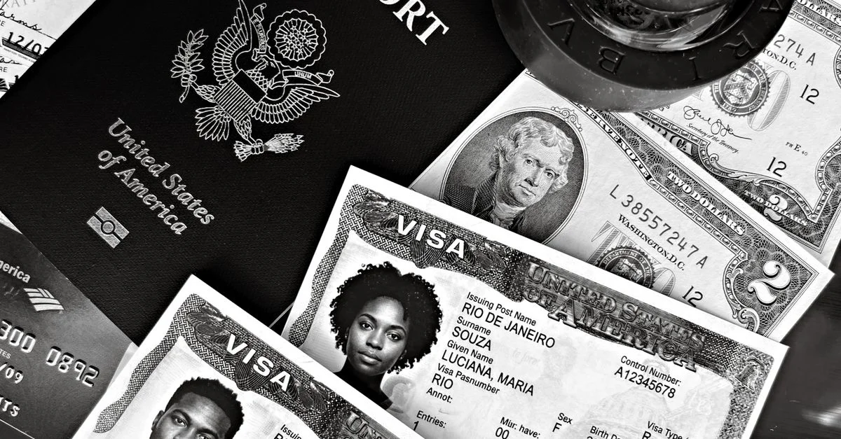 Una composición en blanco y negro de un pasaporte estadounidense, visados y moneda, que muestra artículos esenciales para viajar.