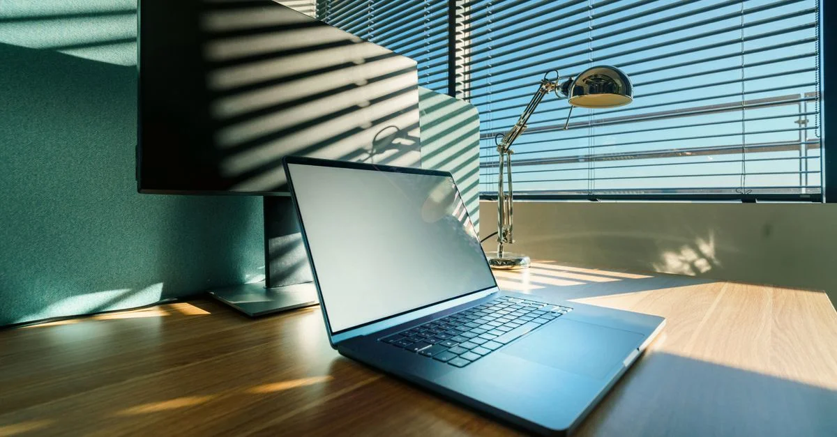 Un escritorio de oficina limpio y soleado con una computadora portátil y un monitor modernos, perfecto para entornos comerciales o corporativos.