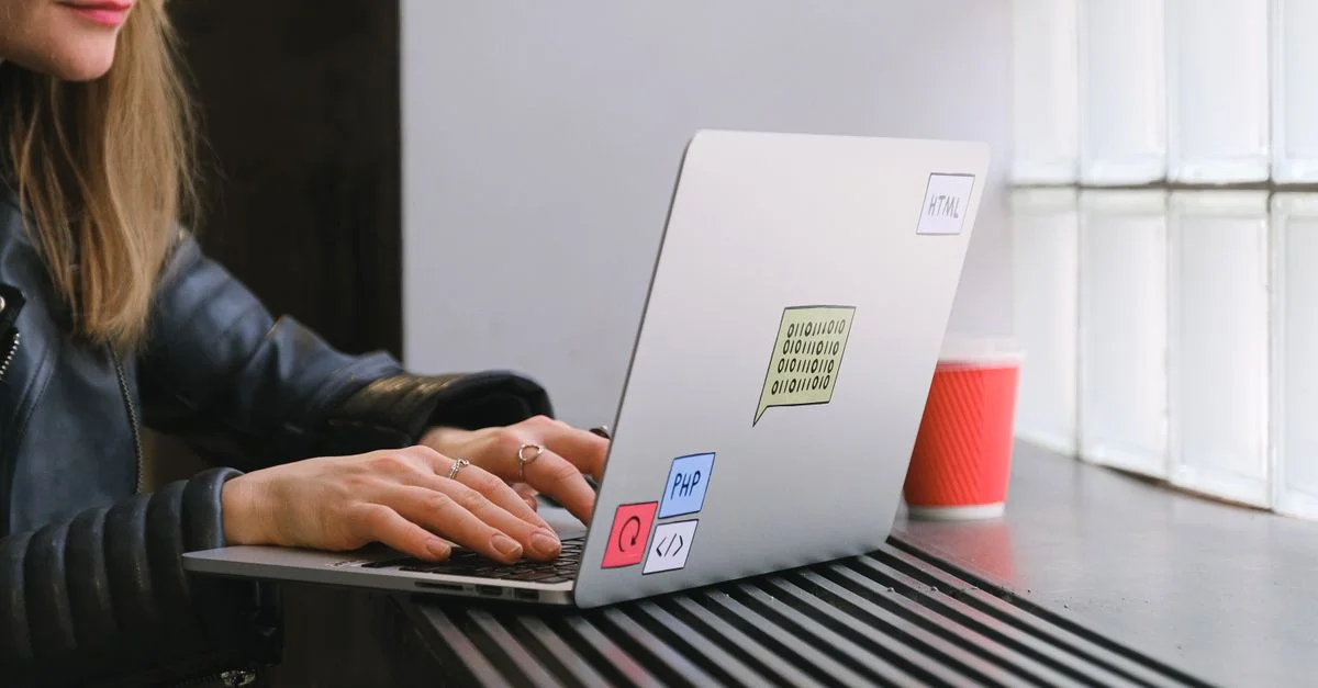 Mujer usando un portátil junto a una ventana en un café con un café. Ideal para temas de tecnología y estilo de vida.
