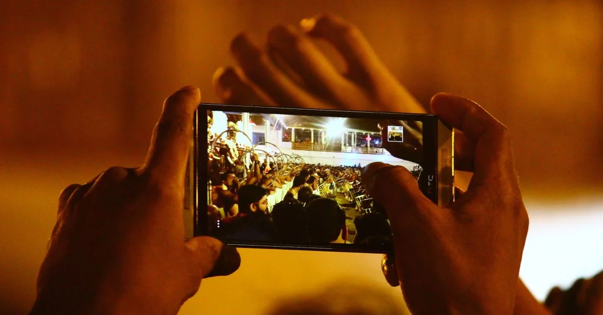 Manos sosteniendo un smartphone capturando una escena de concierto en vivo, destacando el uso de la tecnología moderna.
