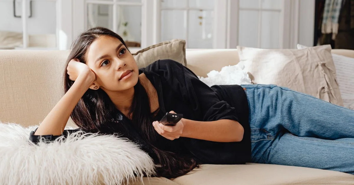 Mujer relajándose en un sofá con el control remoto en la mano, disfrutando de la relajación en interiores.