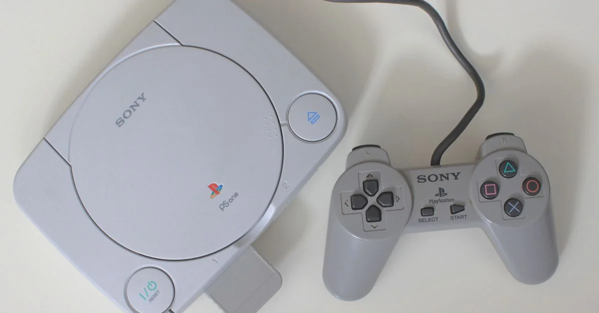 Vista desde arriba de una clásica consola Sony PlayStation con un mando sobre una superficie blanca.