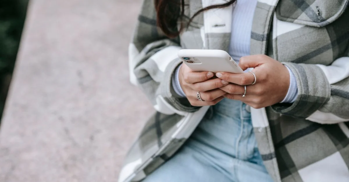 Una mujer utilizando su smartphone mientras está sentada al aire libre, mostrando un estilo de vida moderno y conectividad.