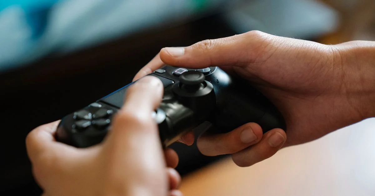 Manos sosteniendo un mando de videojuego en interiores, perfecto para temas de juegos y entretenimiento.