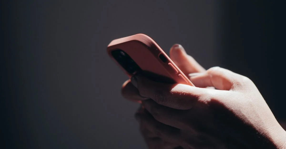 Primer plano de manos sosteniendo un smartphone con poca luz, mostrando actividad de enviar mensajes o navegar.