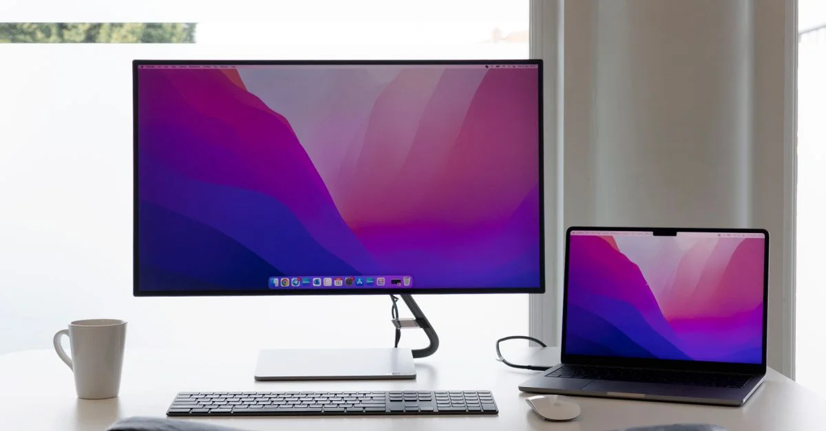 Espacio de trabajo minimalista con dos monitores, teclado y una laptop sobre un escritorio limpio.