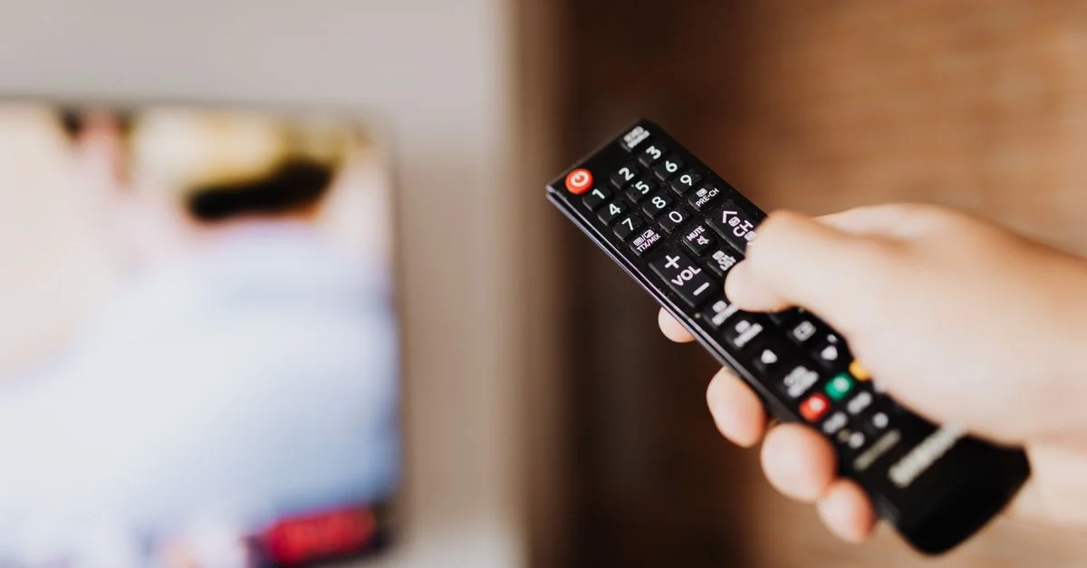 Primer plano de una persona usando un control remoto de TV con un fondo borroso en interiores.