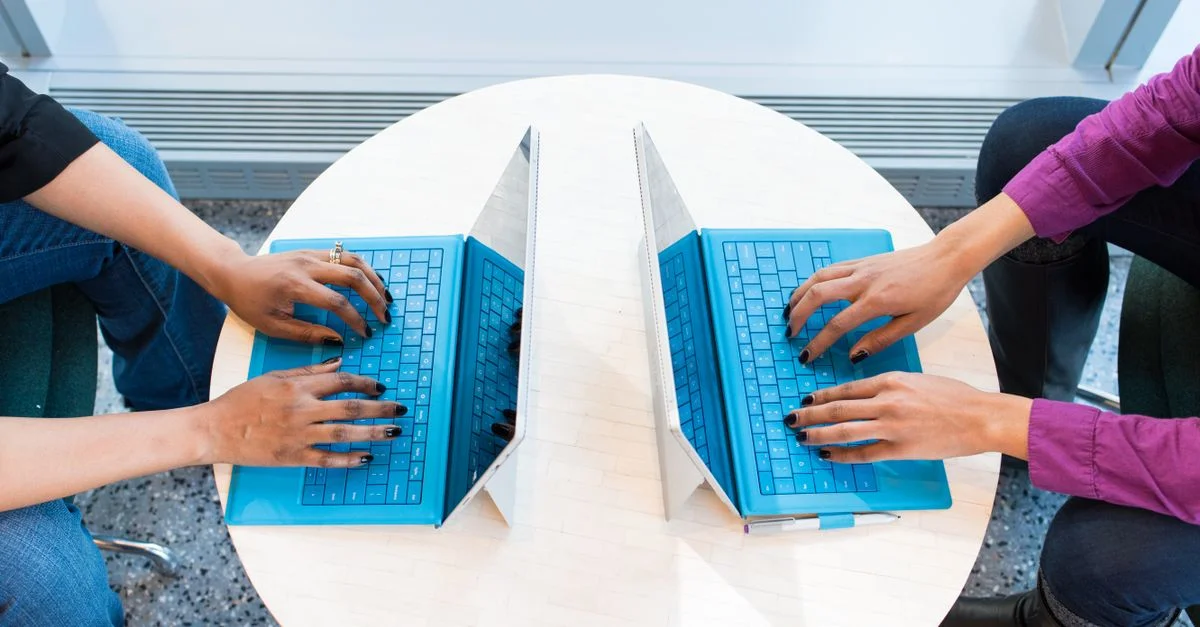 Dos personas trabajando en portátiles azules en una mesa redonda, enfocándose en el trabajo en equipo y la tecnología.