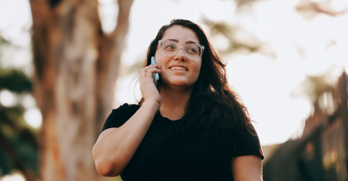 Mujer feliz con gafas sonríe mientras habla por un smartphone al aire libre.