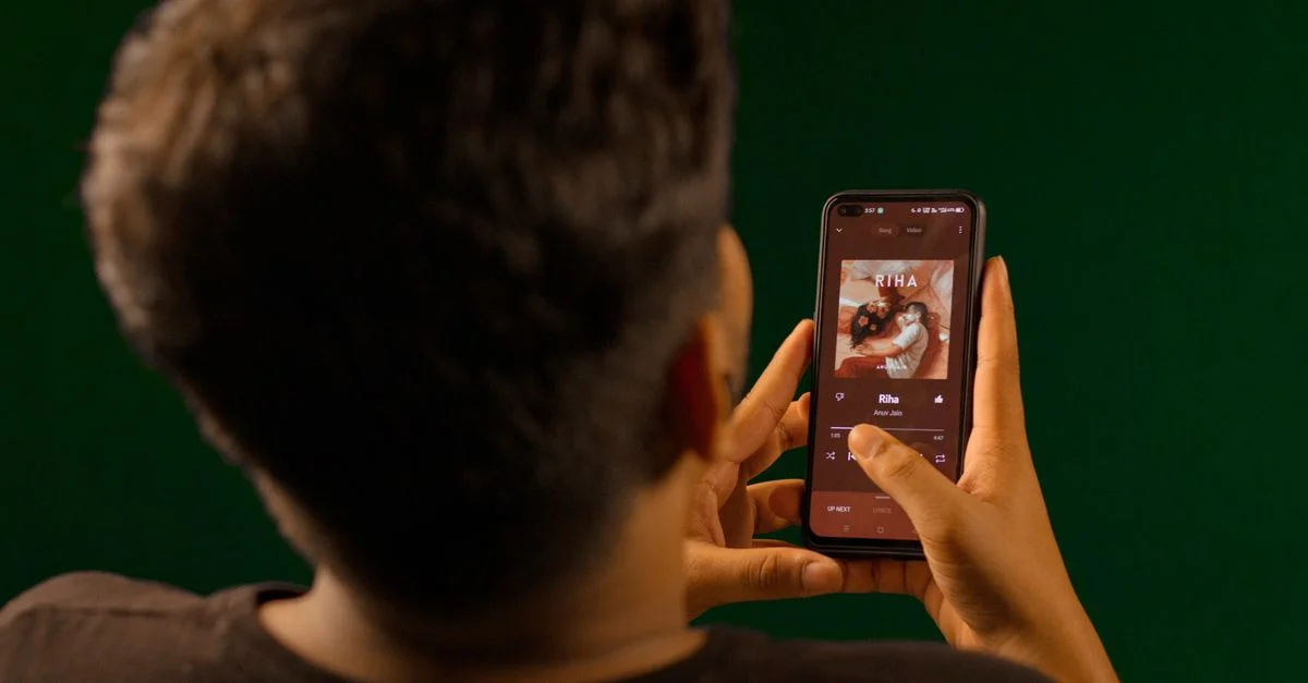 Una persona usando un smartphone para transmitir música desde una aplicación de servicio de streaming en interiores.